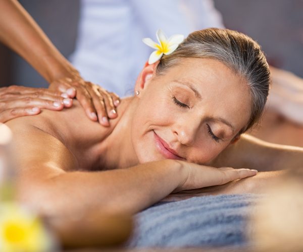 Woman lying on a spa bed and getting a relaxing massage. Serene mature woman having oil massage on her back. Portrait of senior woman with closed eyes having spa treatment.